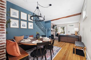 A dining area with a round table set for four, a staircase leading to an upper level, and a kitchen visible through an open door. - Charming 2BR Retreat | Fully Equipped | Near German Village | 30+ nights (Columbus)
