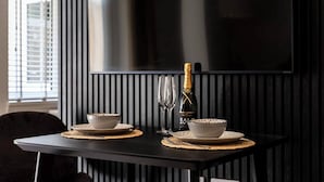A dining table with two bowls, a bottle of champagne, and two glasses, set against a dark wall with vertical slats. - Pelican House No.3 | Luxury Apartment | Walk to the Beach | Bournemouth Centre (Bournemouth, Christchurch and Poole)