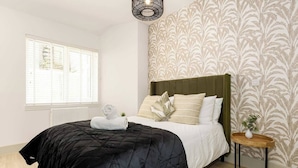 A hotel room with a bed, a bedside table with a vase, and a window with blinds. - Pelican House No.3 | Luxury Apartment | Walk to the Beach | Bournemouth Centre (Bournemouth, Christchurch and Poole)