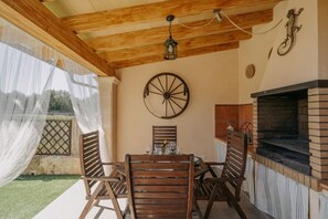 Eine Terrasse im Freien mit Holztisch und -stühlen, einem Backofen aus Ziegeln und einem dekorativen Wagenrad an der Wand.