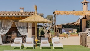 Een zwembadgedeelte met ligbedden, een rieten parasol en een eethoek met tuinmeubilair.