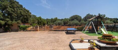 Un espacio al aire libre con mesa de ping pong, un arenero y un jardín cercado.