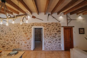 Ein rustikales Interieur mit freiliegenden Steinwänden, Holzbalken, einem Essbereich mit Tisch und Stühlen sowie einer Treppe.