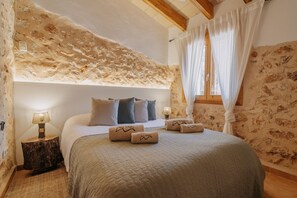 Ein Schlafzimmer mit Steinwand, einem Bett mit Kissen, einem Nachttisch mit Lampe und einem Fenster mit Vorhängen.