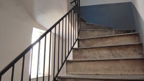 Uma escadaria com corrimão de metal preto, degraus de madeira e parede azul no topo.