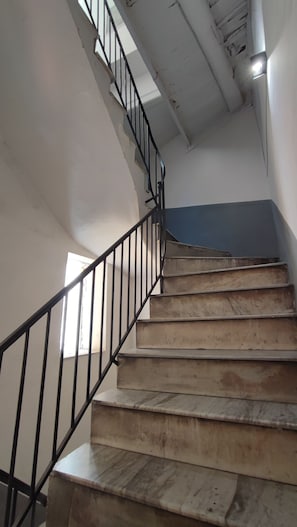 Una escalera con barandilla de metal negro, escalones de madera y una pared azul en la parte superior.