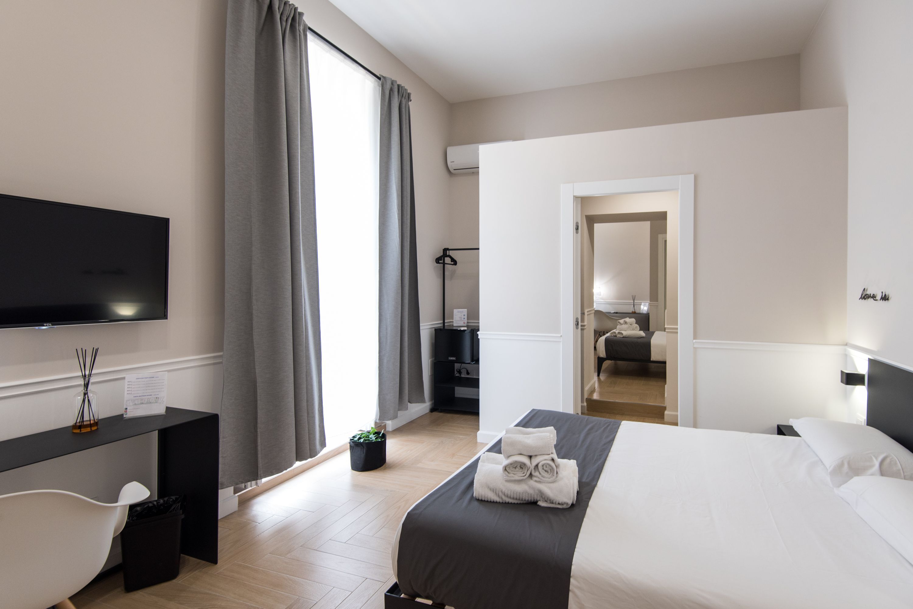 A modern hotel room with a bed, a desk, a television, and a bathroom visible through an open door.