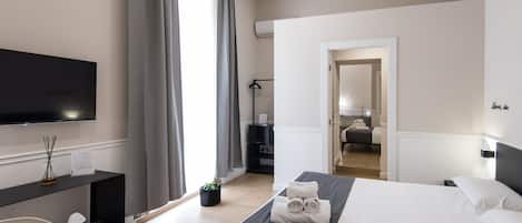 A modern hotel room with a bed, a desk, a television, and a bathroom visible through an open door.