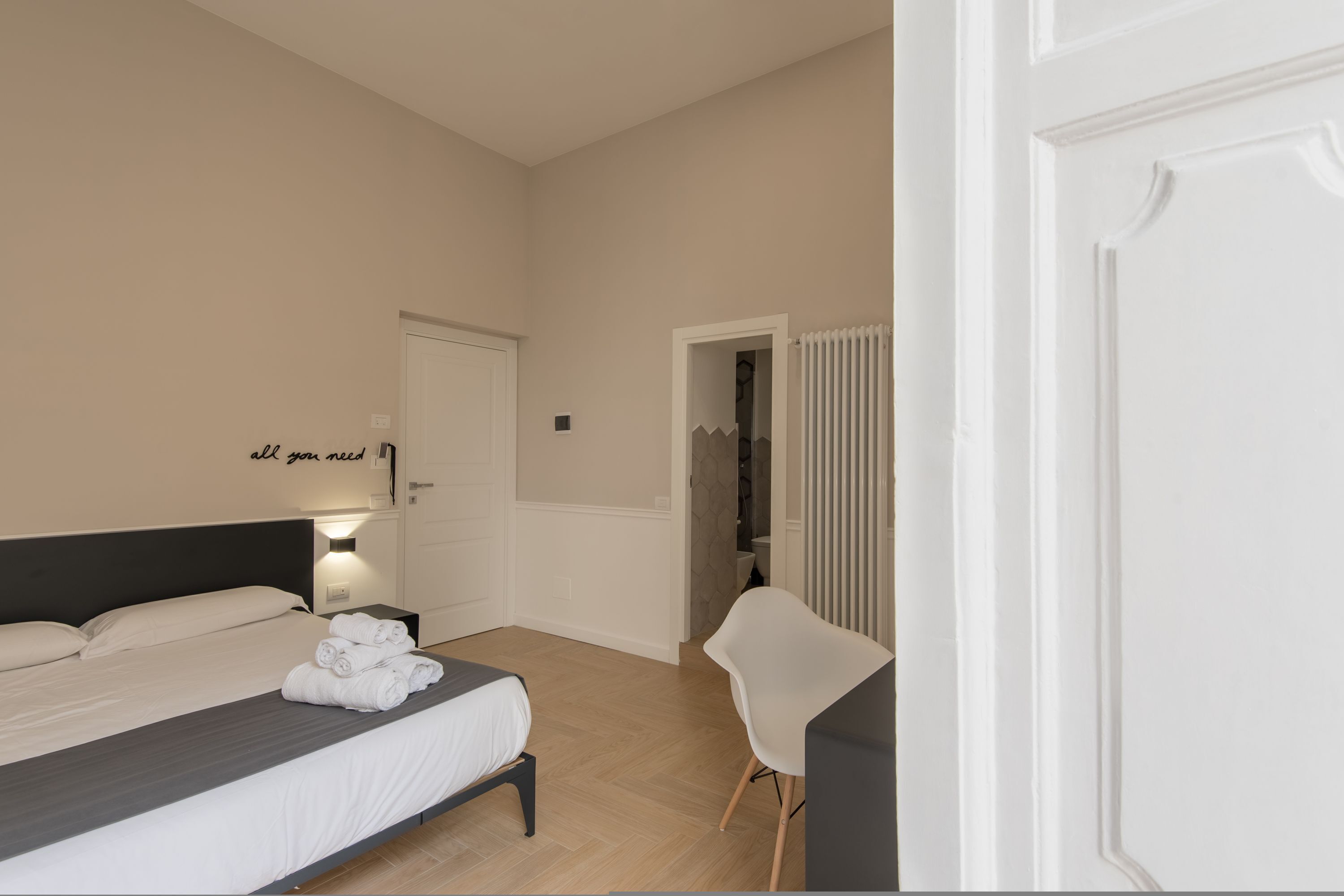 A hotel room with a bed, a chair, a bathroom, and a door with a sign.