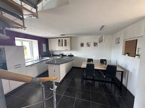 A modern kitchen with a dining area, featuring a central island, black tiled flooring, and a ceiling with a light fixture. - Country House (Langoat)