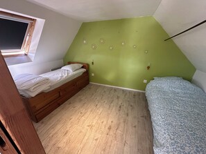 A small, single-room apartment with a sloped ceiling, a wooden bed, a second bed with a patterned bedspread, and a window with a view. - Country House (Langoat)