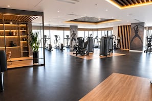 Ein modernes Fitnessstudio mit unterschiedlichen Trainingsgeräten, großen Fenstern und einem hölzernen Empfangsbereich.