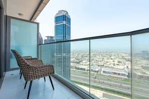 Ein Balkon mit Korbstühlen, einer Glastrennwand und Blick auf eine Stadtlandschaft, darunter ein hohes, blaues Gebäude.