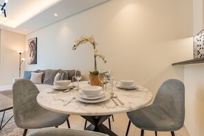 Comedor con una mesa redonda dispuesta para cuatro personas, rodeado de sillas grises, y un florero con orquídeas blancas en el centro.