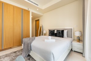 A modern bedroom with a large bed, a nightstand, a bedside table, a mirror, and a wardrobe. - Prime High-Floor 2BR Retreat with Stunning Burj Khalifa Views, Near the Metro (Dubai)