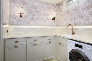 A modern kitchen with a built-in washing machine, white cabinetry, and decorative wall sconces. - Dimora Dell’Arcangelo La Loggia (Lucca)
