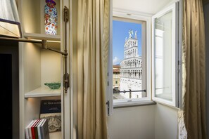 A room with a window overlooking a historic building, a bookshelf with books, and a decorative vase. - Dimora Dell’Arcangelo La Loggia (Lucca)