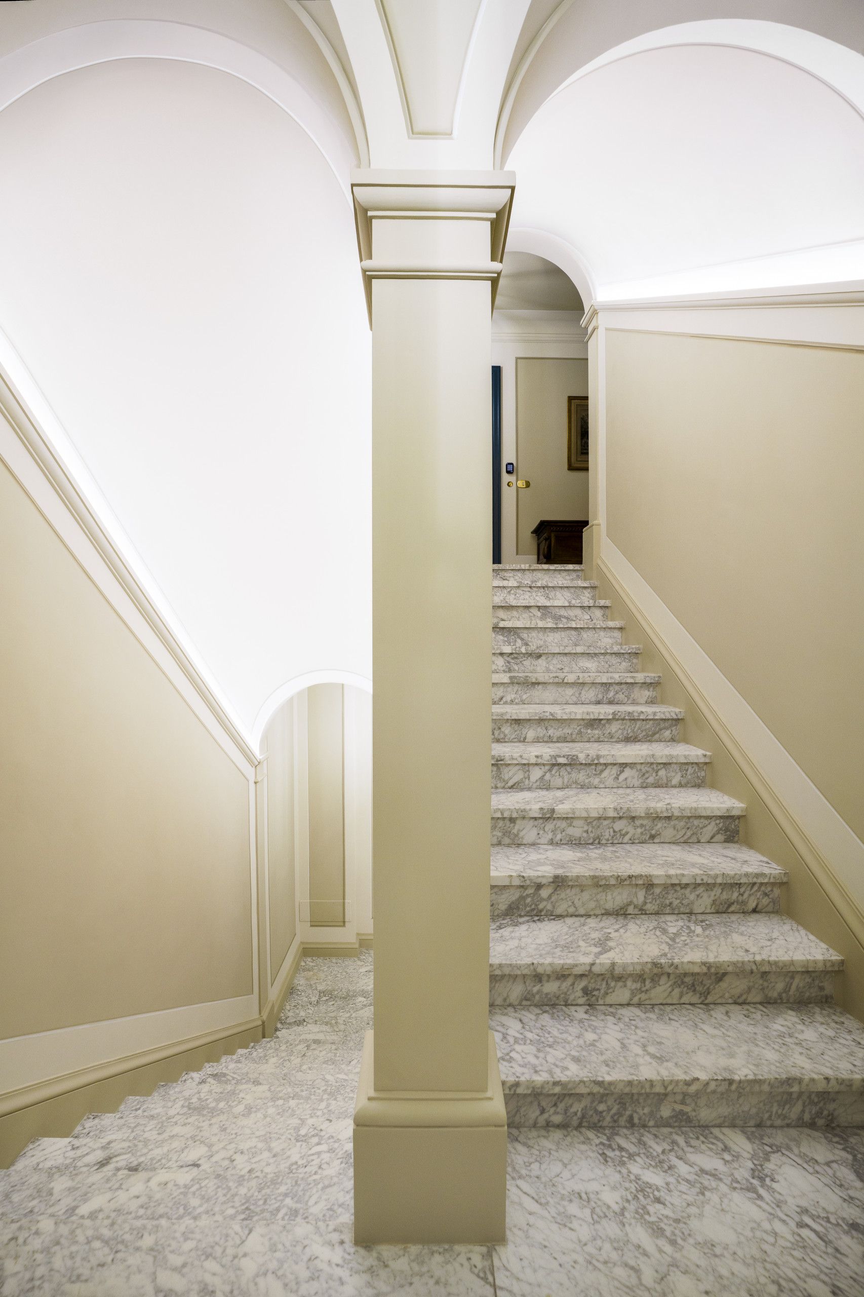 Un escalier avec des marches en marbre et une colonne centrale, menant à une porte située en haut.