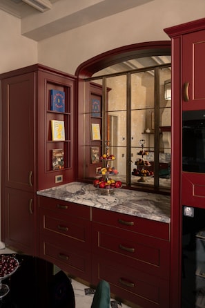 A kitchen with marble countertops, red cabinetry, and a fruit display. - Dimora Dell’Arcangelo Piano Nobile (Lucca)