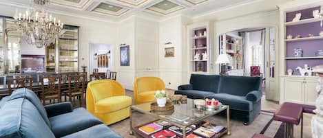 A spacious living room with a high ceiling, a chandelier, and a variety of seating options including sofas and chairs.