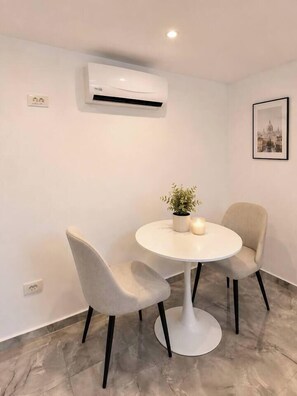 A room with a round table, two chairs, an air conditioner, a wall socket, a framed picture, and a potted plant. - Modern & Elegant Apartment | King Bed (Bucharest)