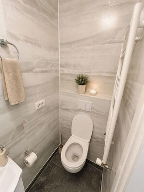 A compact bathroom with a toilet, a towel rack, a small potted plant, and a light fixture. - Modern & Elegant Apartment | King Bed (Bucharest)