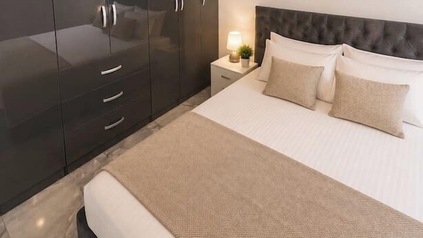 Una camera da letto con un letto grande, un armadio scuro, un comodino con una lampada e un lampadario.
