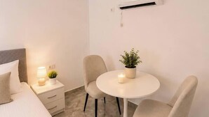 Una camera d'albergo con un letto, un comodino, una lampada, due sedie, un tavolino con una pianta e un condizionatore.