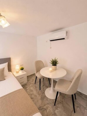 A hotel room with a bed, bedside table, lamp, two chairs, a small table with a plant, and an air conditioning unit. - Modern & Elegant Apartment | King Bed (Bucharest)