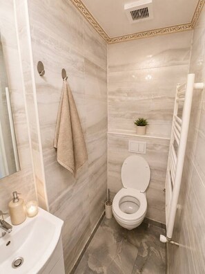 A bathroom with a toilet, sink, towel rack, and a small potted plant. - Modern & Elegant Apartment | King Bed (Bucharest)