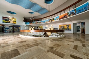 Een ruime lobby met een centraal gelegen receptiebalie, houten vloeren en een hoog plafond met blauwe details.