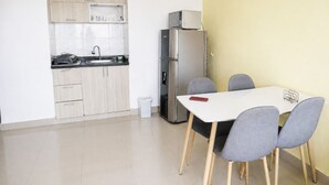 Cocina compacta con refrigerador, microondas y pileta. Hay un bote pequeño de basura y una mesa con cuatro sillas.