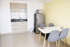 A compact kitchen with a refrigerator, microwave, and sink. There is a small trash bin and a table with four chairs. - Encantador Apartamento Frente a la Playa (Cartagena de Indias)