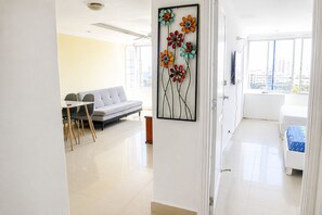 Een moderne woonkamer met een bank, eettafel en stoelen, een groot raam met uitzicht op de stad, en een kunstwerk aan de muur.