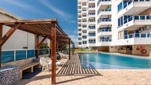 Un área de piscina con una pérgola de madera, sillas de descanso y un suelo de baldosas.