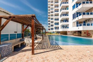 A pool area with a wooden pergola, lounge chairs, and a tiled deck. - Encantador Apartamento Frente a la Playa (Cartagena de Indias)