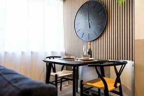 En matplats med ett bord, stolar, en stor väggklocka och en flaska champagne.