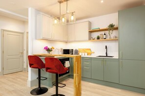 A modern kitchen with a wooden island, two red bar stools, a built-in oven, and a wine bottle on the shelf. - Pelican House No.6 | Luxury Apartment | Walk to the Beach | Bournemouth Centre (Bournemouth, Christchurch and Poole)