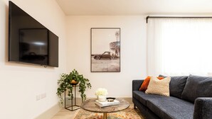 A living room with a flat-screen TV, a framed picture, a sofa, a coffee table, and a plant. - Pelican House No.6 | Luxury Apartment | Walk to the Beach | Bournemouth Centre (Bournemouth, Christchurch and Poole)