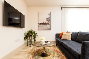 Ett vardagsrum med en platt-TV, en inramad tavla, en soffa, ett soffbord och en växt.