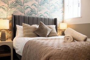 En snyggt bäddad säng med en mörk sänggavel, flera kuddar och en hoprullad handduk.
