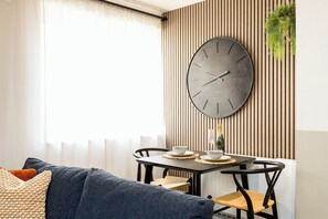 Ein modernes Wohnzimmer mit Essbereich, mit einer großen Wanduhr, einem Sofa und einem Tisch für zwei Personen.