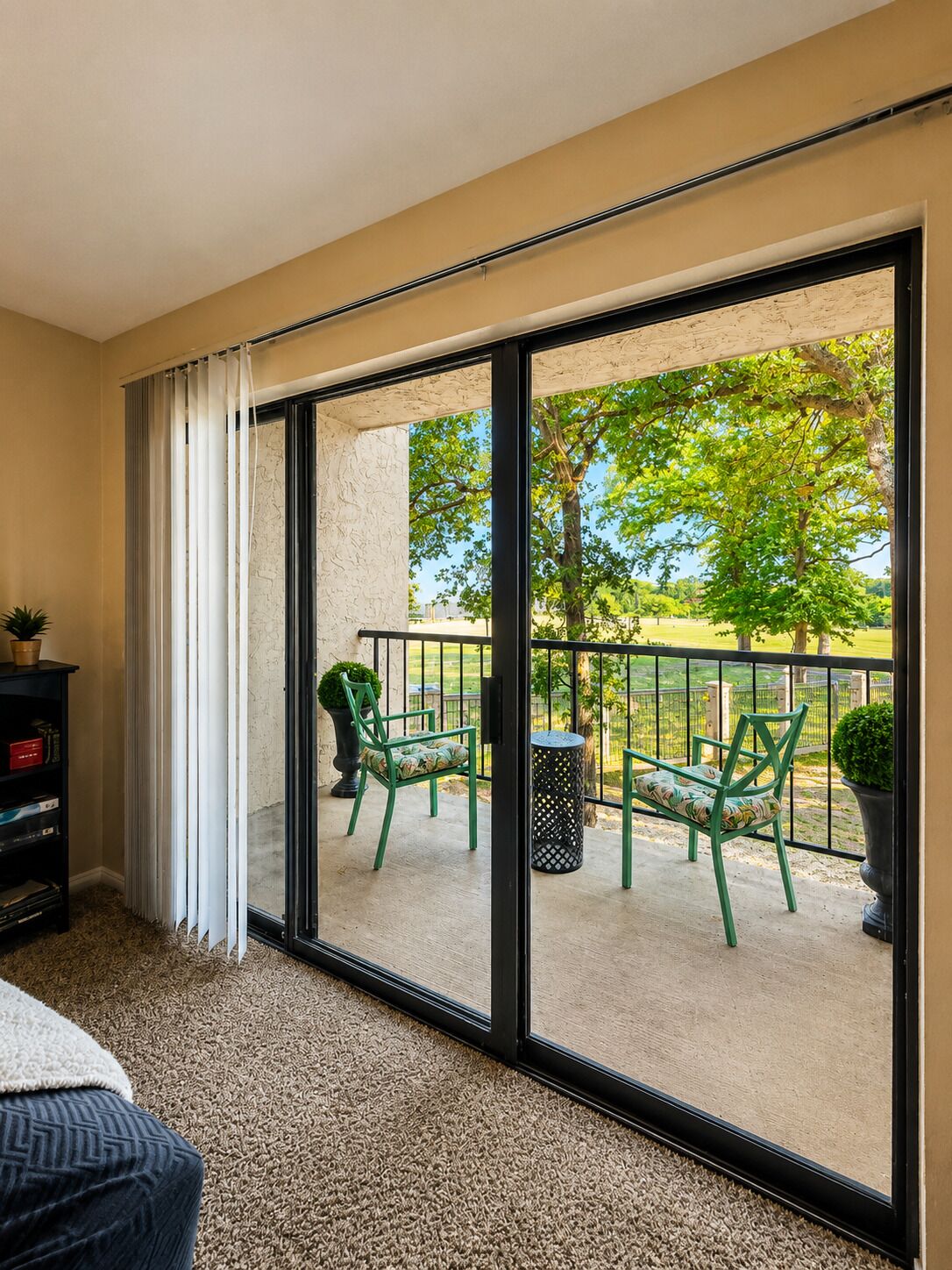 A room with a sliding glass door leading to an outdoor area with chairs and a view of a green landscape.
