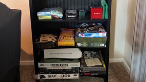 A bookshelf with various board games and a toilet paper holder.