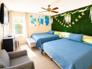 Ein Schlafzimmer mit zwei Betten, einem Deckenventilator, Kunstwerken an der Wand und einer grünen Wanddekoration.