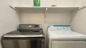 A compact laundry area with a stainless steel dryer and a white front-loading washer, both placed under a white shelf.
