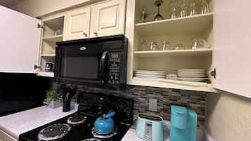 A kitchen with a black stove, a microwave, and a toaster. There are cabinets above the stove and a shelf with glassware.