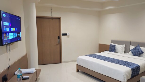 A hotel room with a bed, a TV mounted on the wall, a bedside table with a bottle and a remote control, and a door. - Hotel Centrum (Wadhwan)