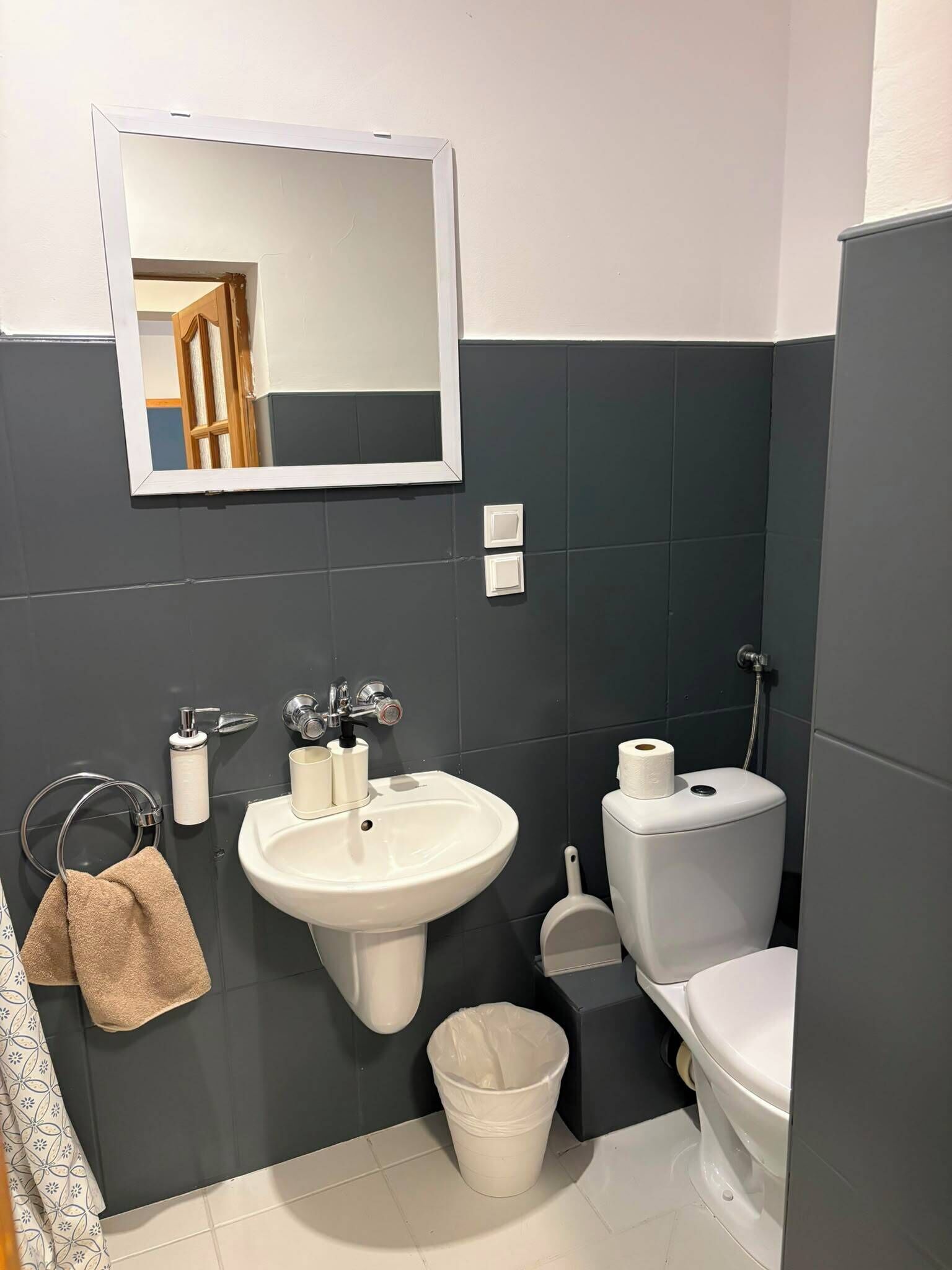 Un baño con lavamanos blanco, inodoro, espejo y toallero.