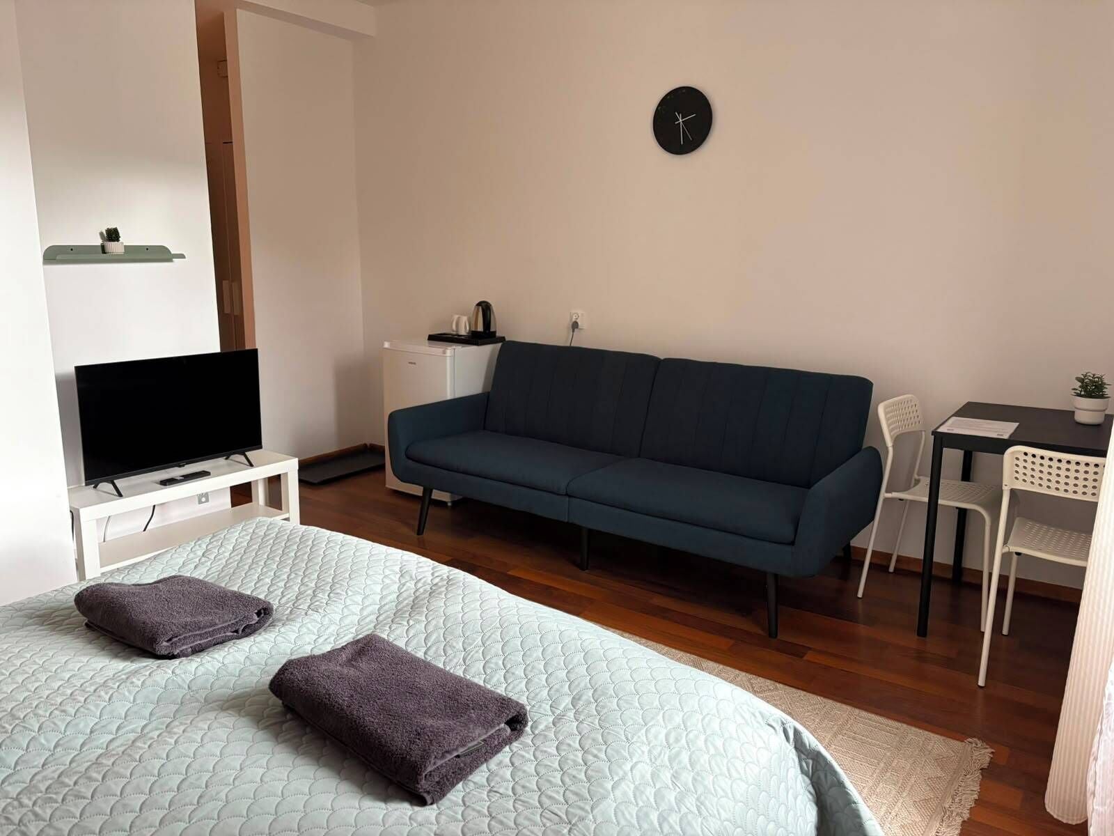 A bedroom with a bed, a television, a sofa, a desk, and a clock on the wall.